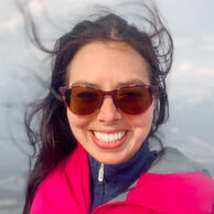 A smiling autistic founder in a pink jacket with her dark hair blowing in the wind